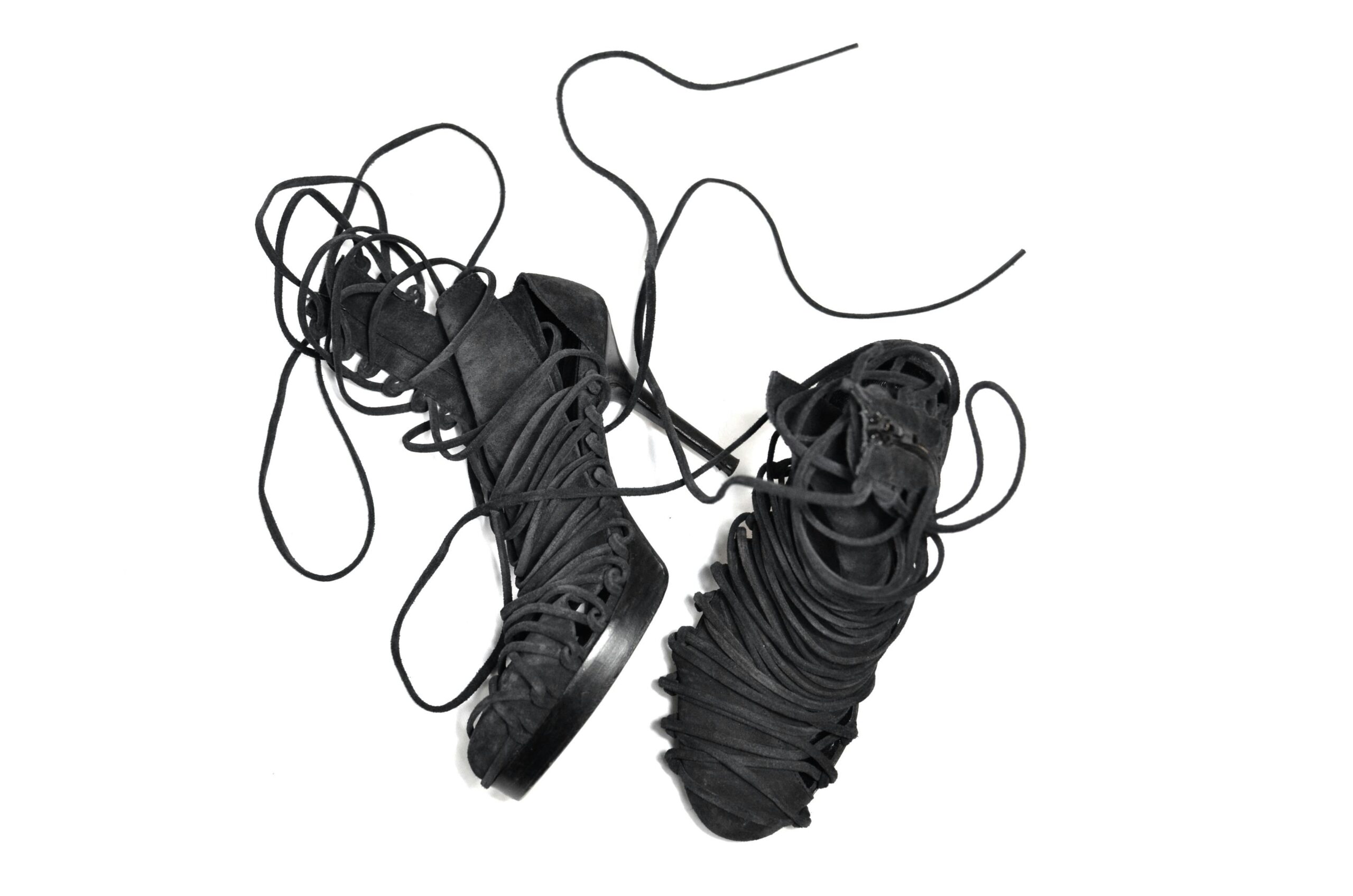 Top view of modern stylish black shoes with high heels and long lacing placed on white surface